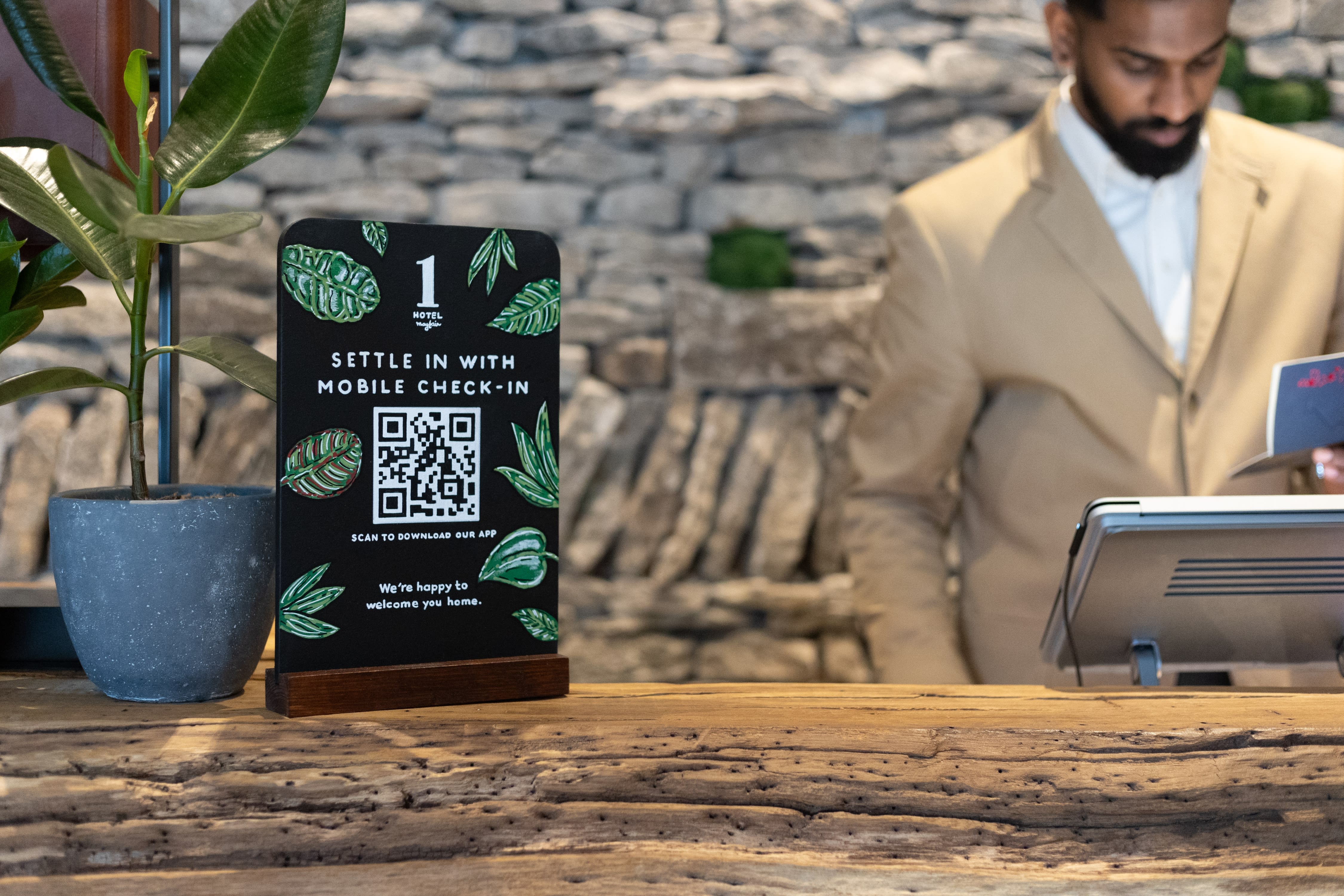 Hand-painted mobile check-in sign on the timber reception desk at 1 Hotel Mayfair.