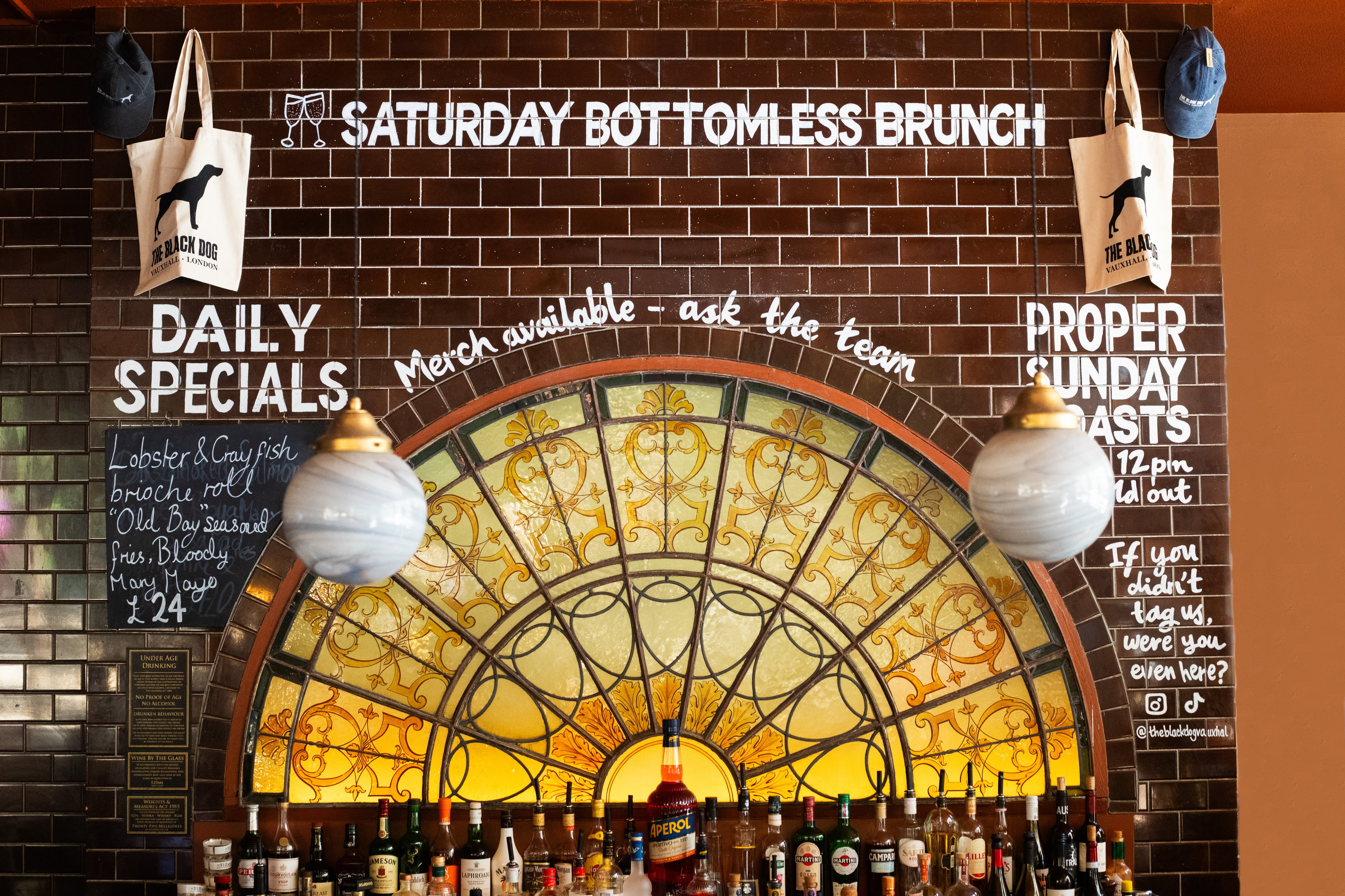 Hand-lettered brunch and Sunday roast blackboards surrounding a stained-glass pub bar.