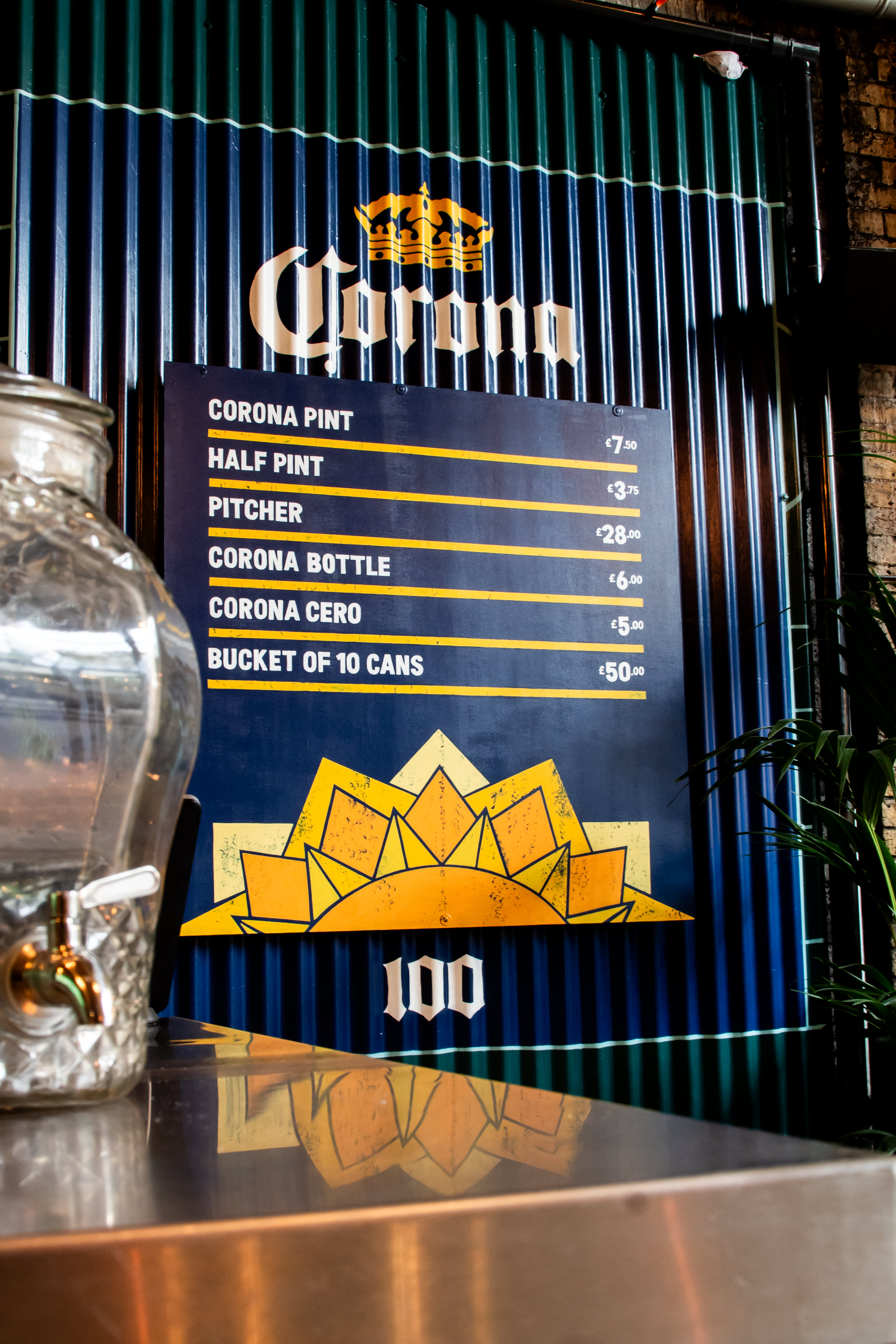 A hand-painted Corona drinks menu on blue corrugated metal at Flat Iron Square.
