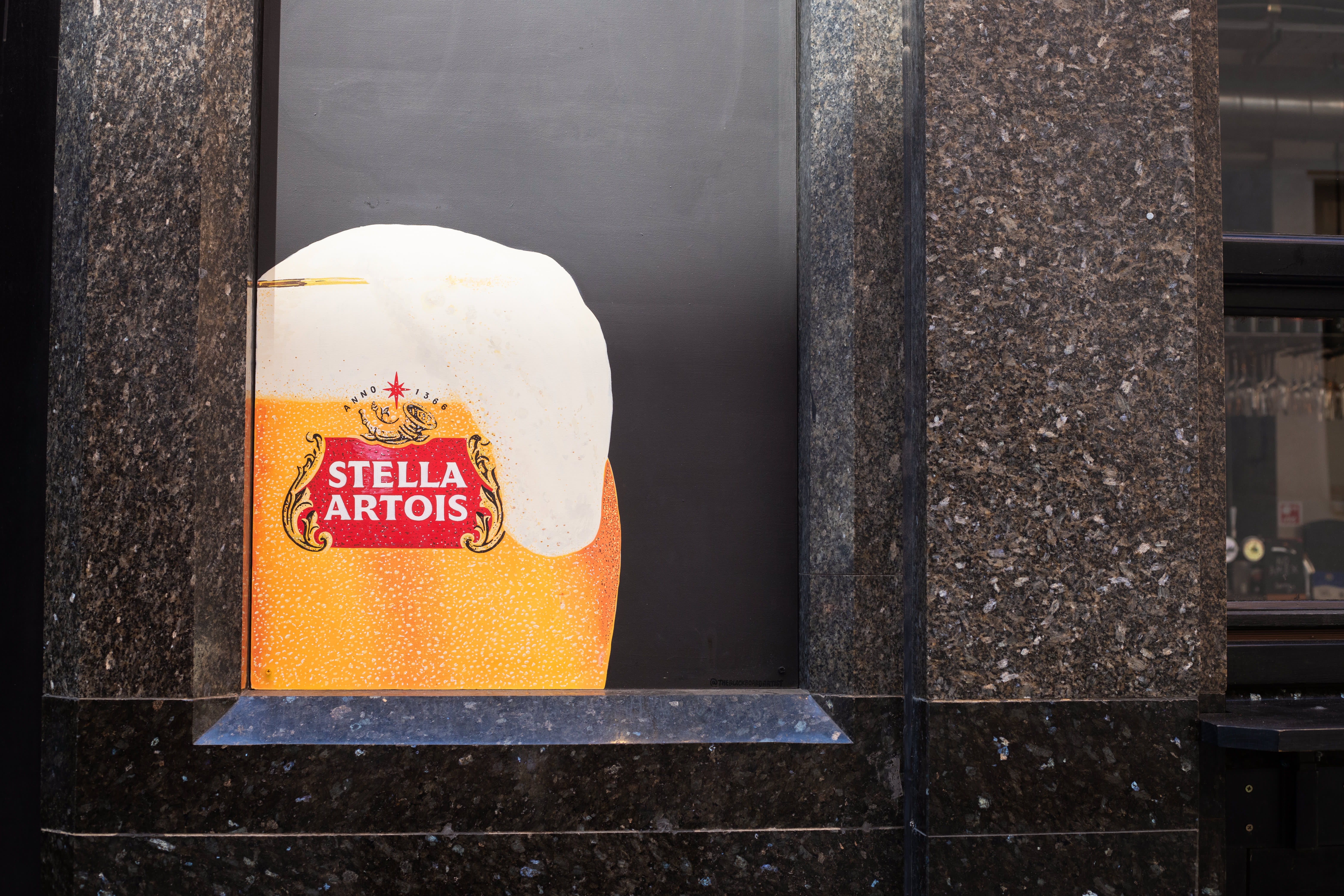 A painted Stella Artois beer glass on a black pub window panel.