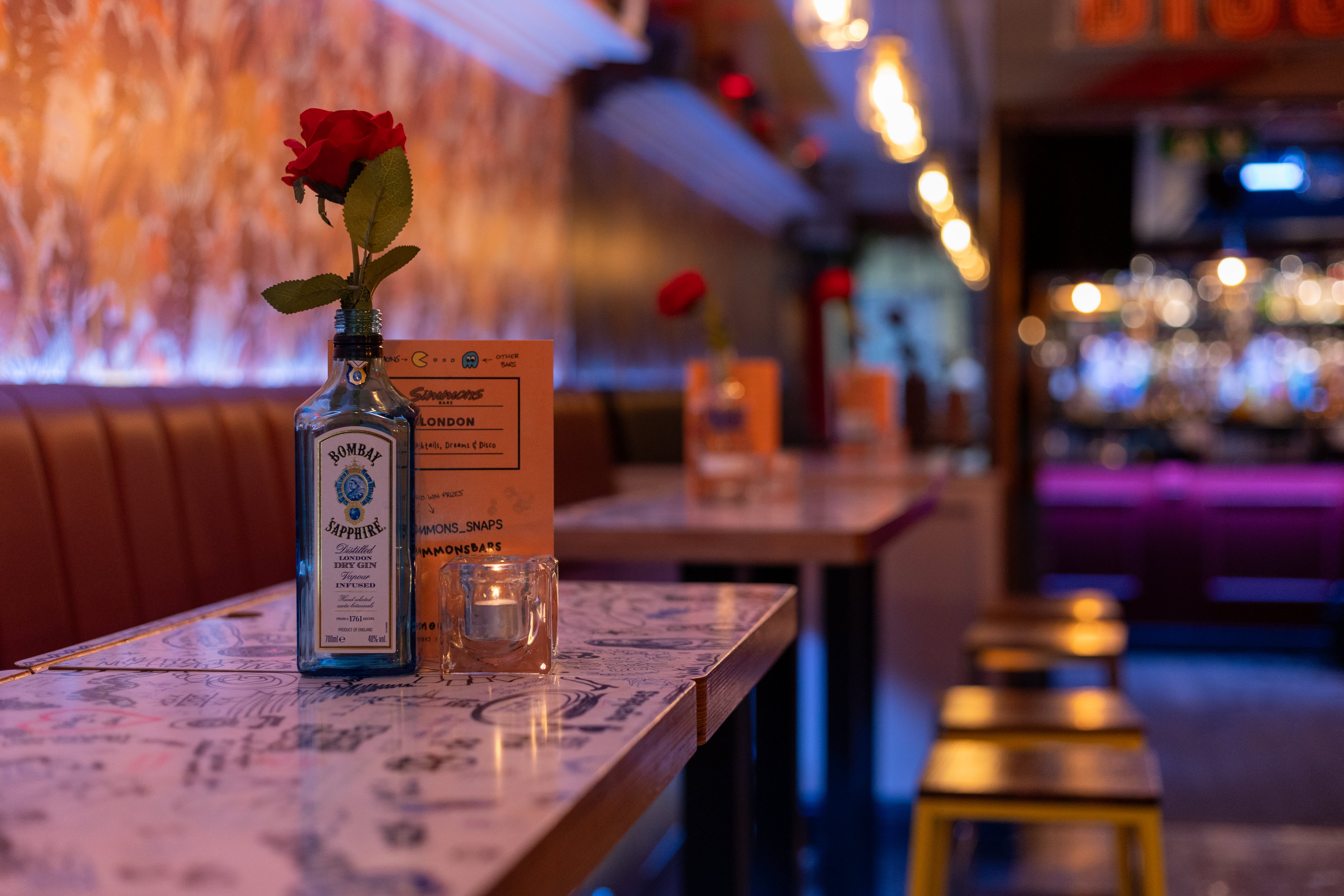 A rose in a bottle on an illustrated tabletop beside Simmons booth seating.