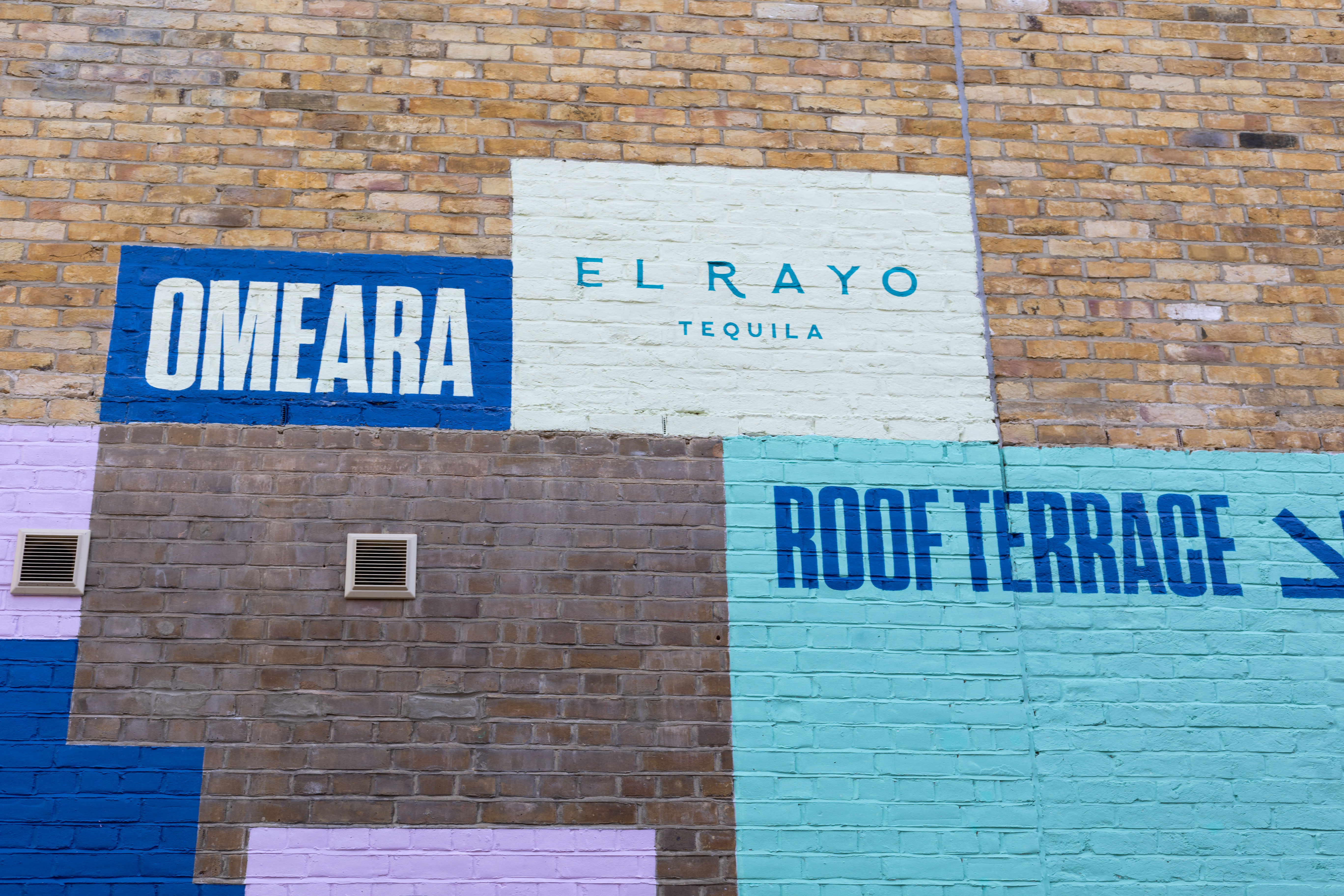 Hand-painted OMEARA, El Rayo and Roof Terrace branding across a colourful brick wall.