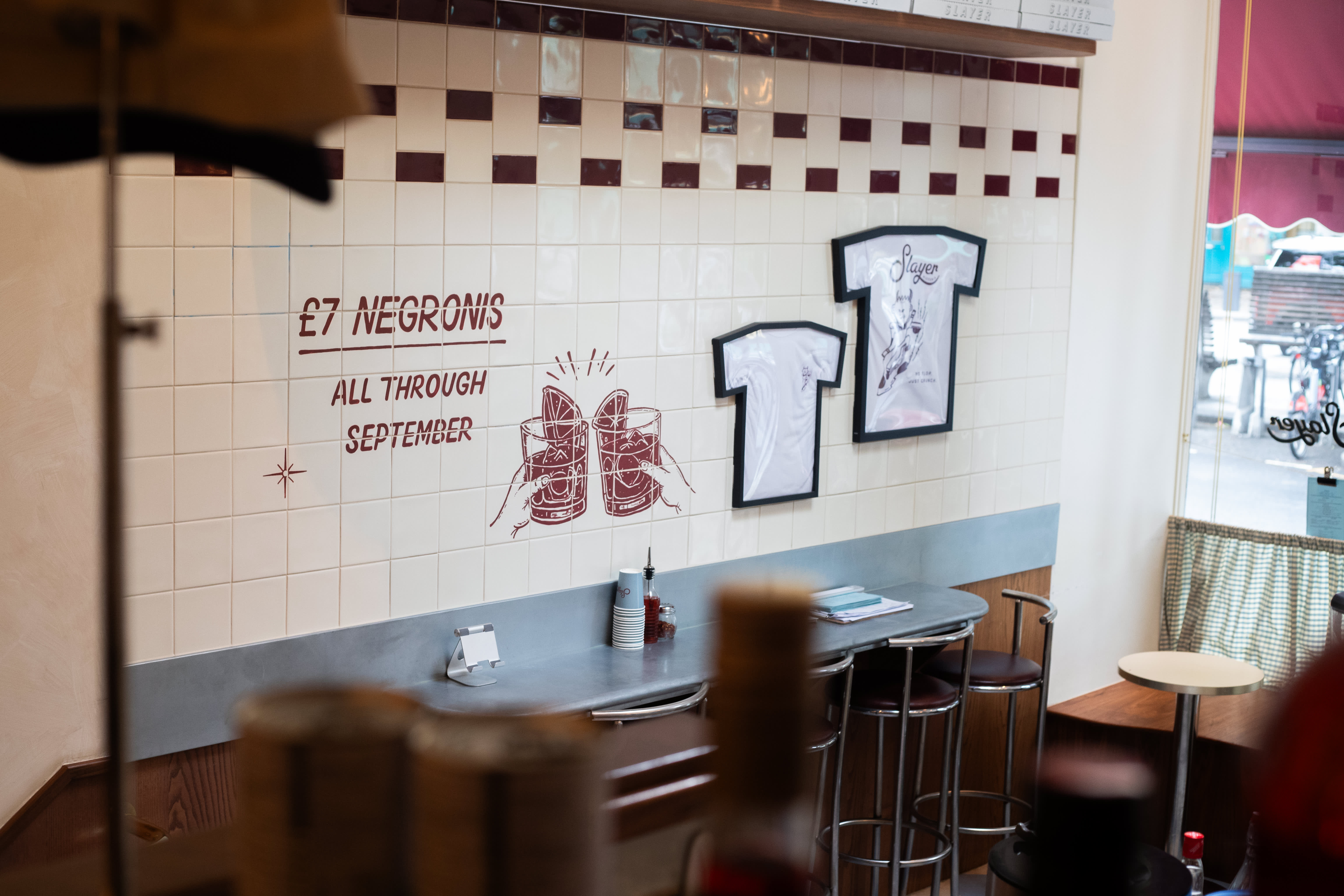 A red hand-painted negroni promotion and framed illustrations on a tiled restaurant wall.