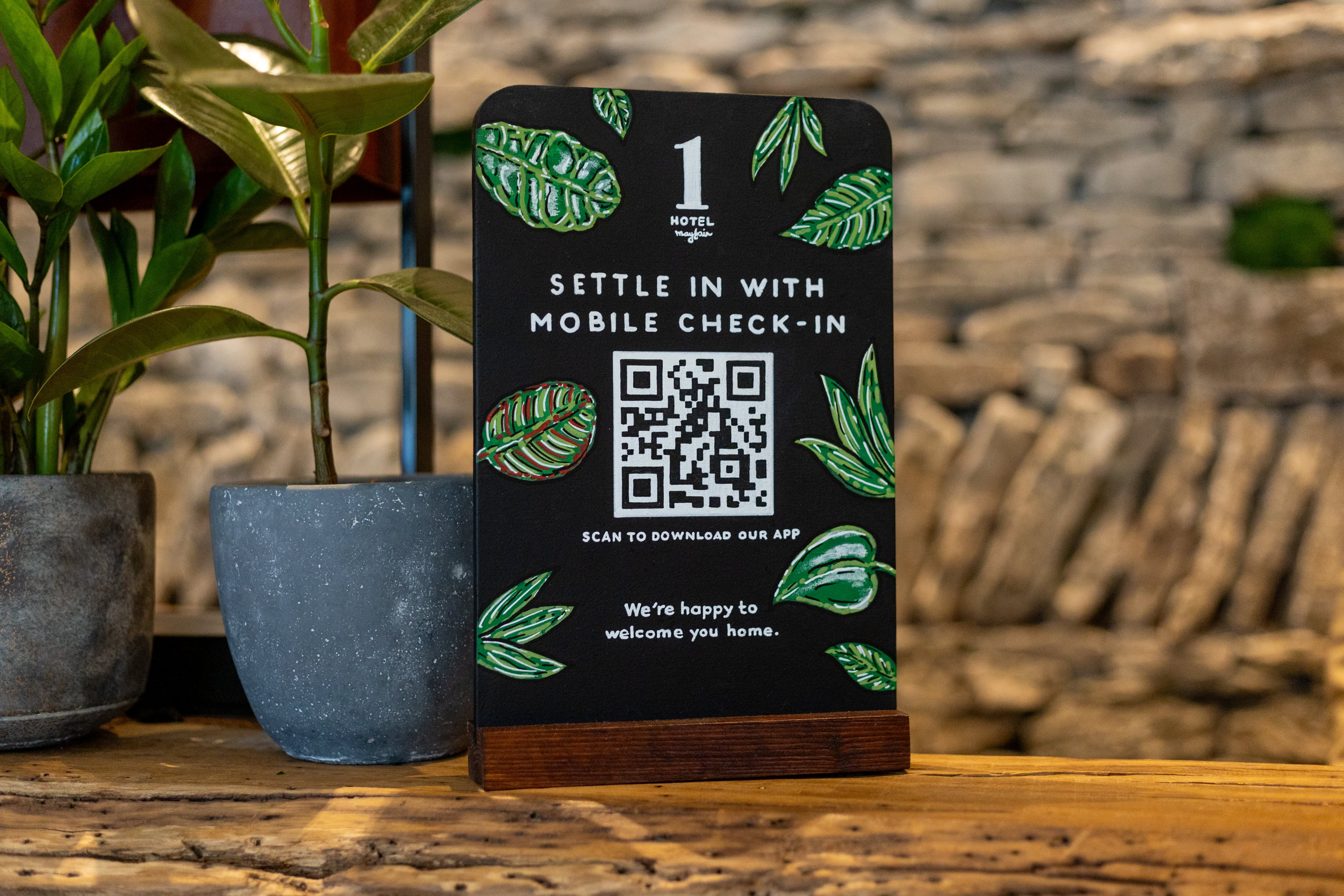 A hand-painted mobile check-in sign with green leaves and a QR code.