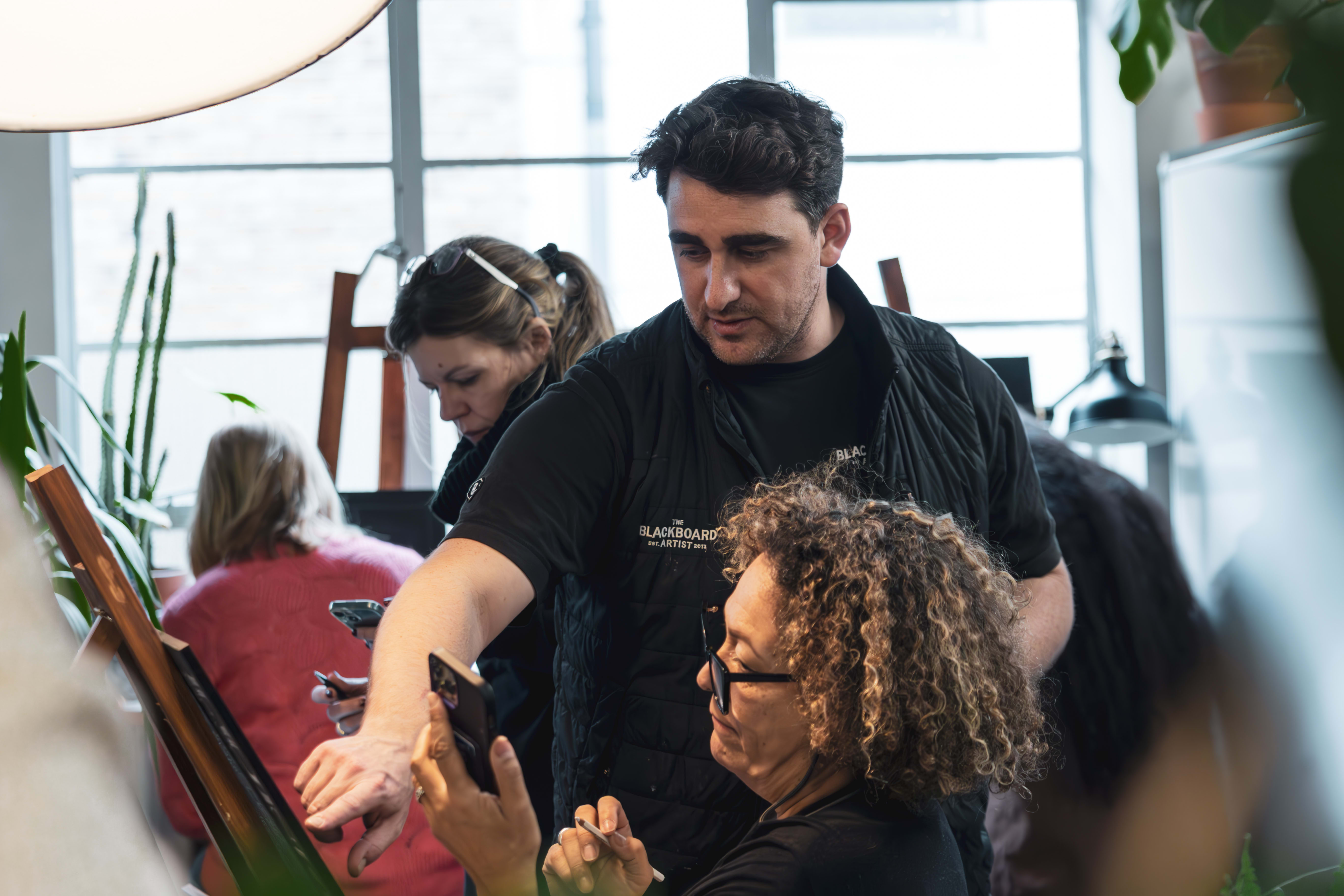 A workshop instructor guiding a participant as she creates her blackboard design.