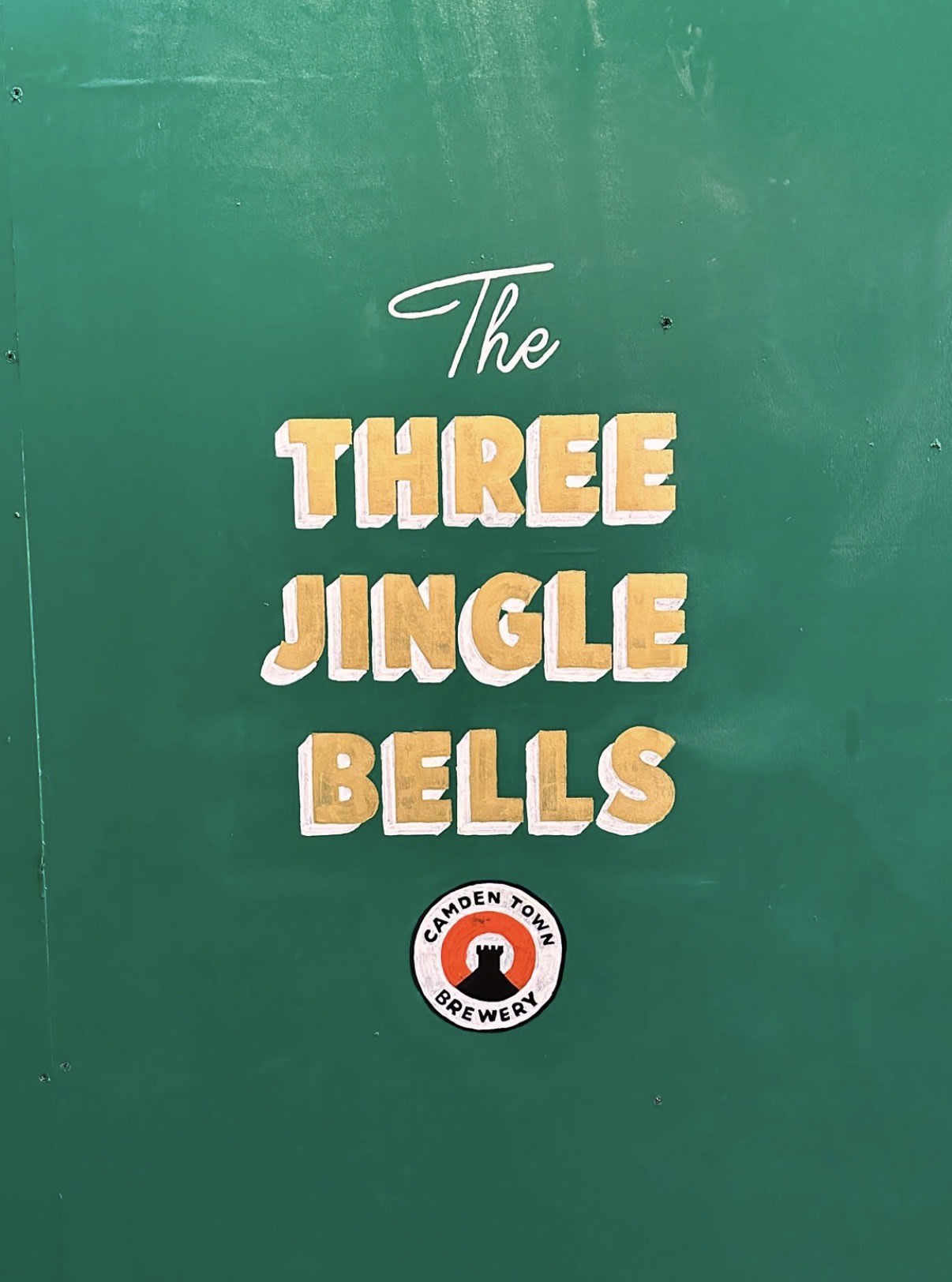 Gold Three Jingle Bells lettering on a green Camden Town Brewery board
