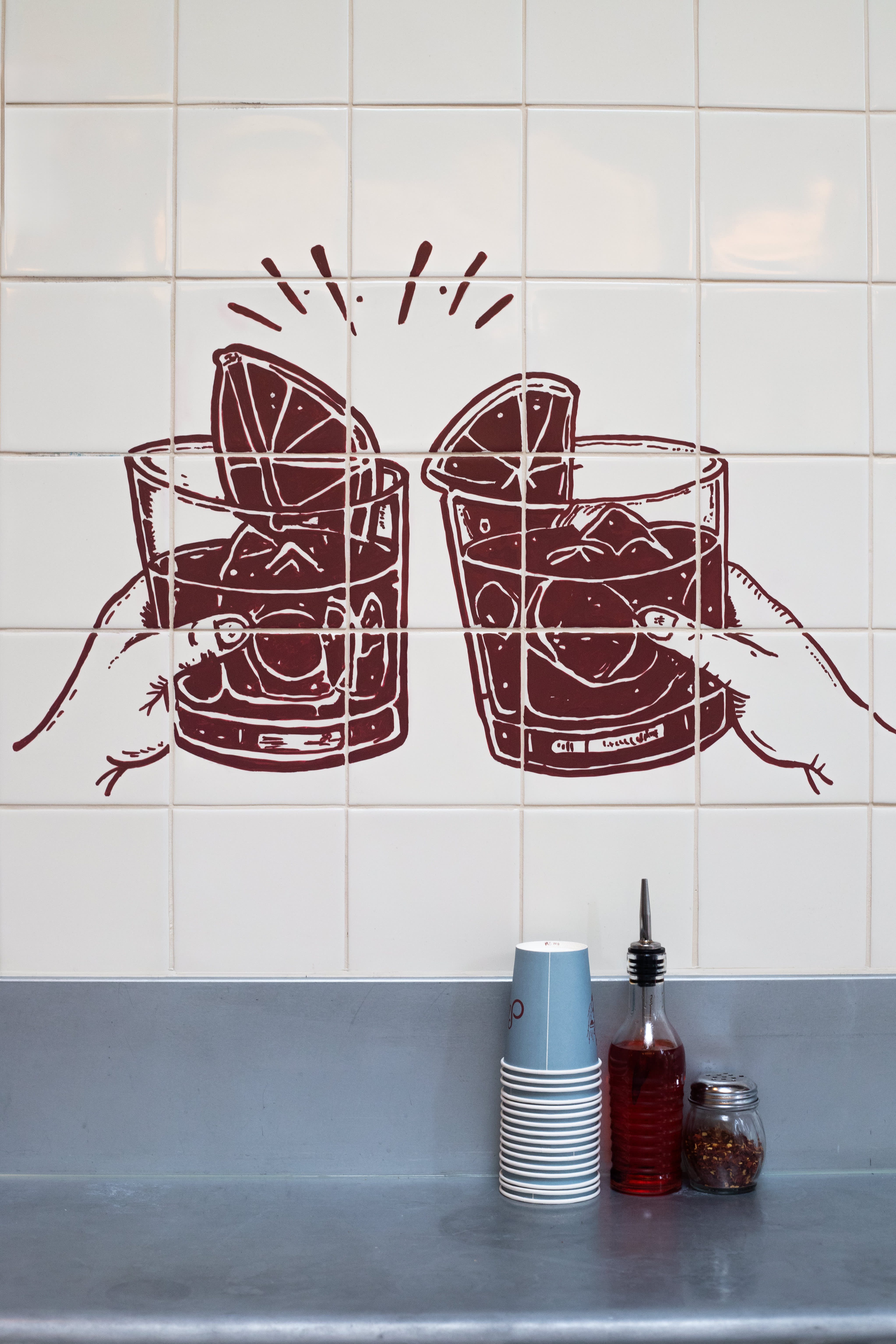 Two cocktail glasses hand-painted in red on a white tiled wall.