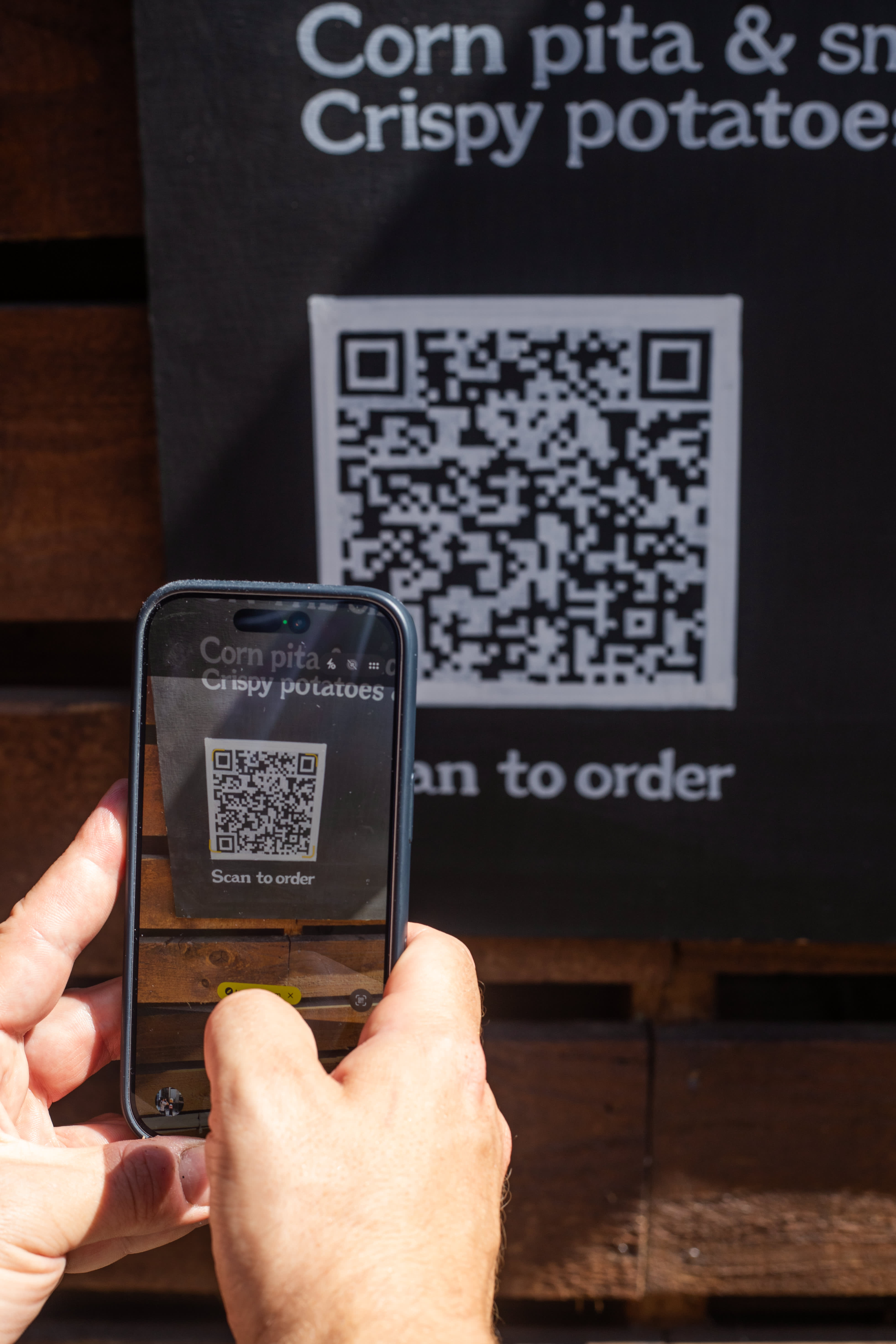 A guest scanning a QR code beside a hand-lettered food menu.