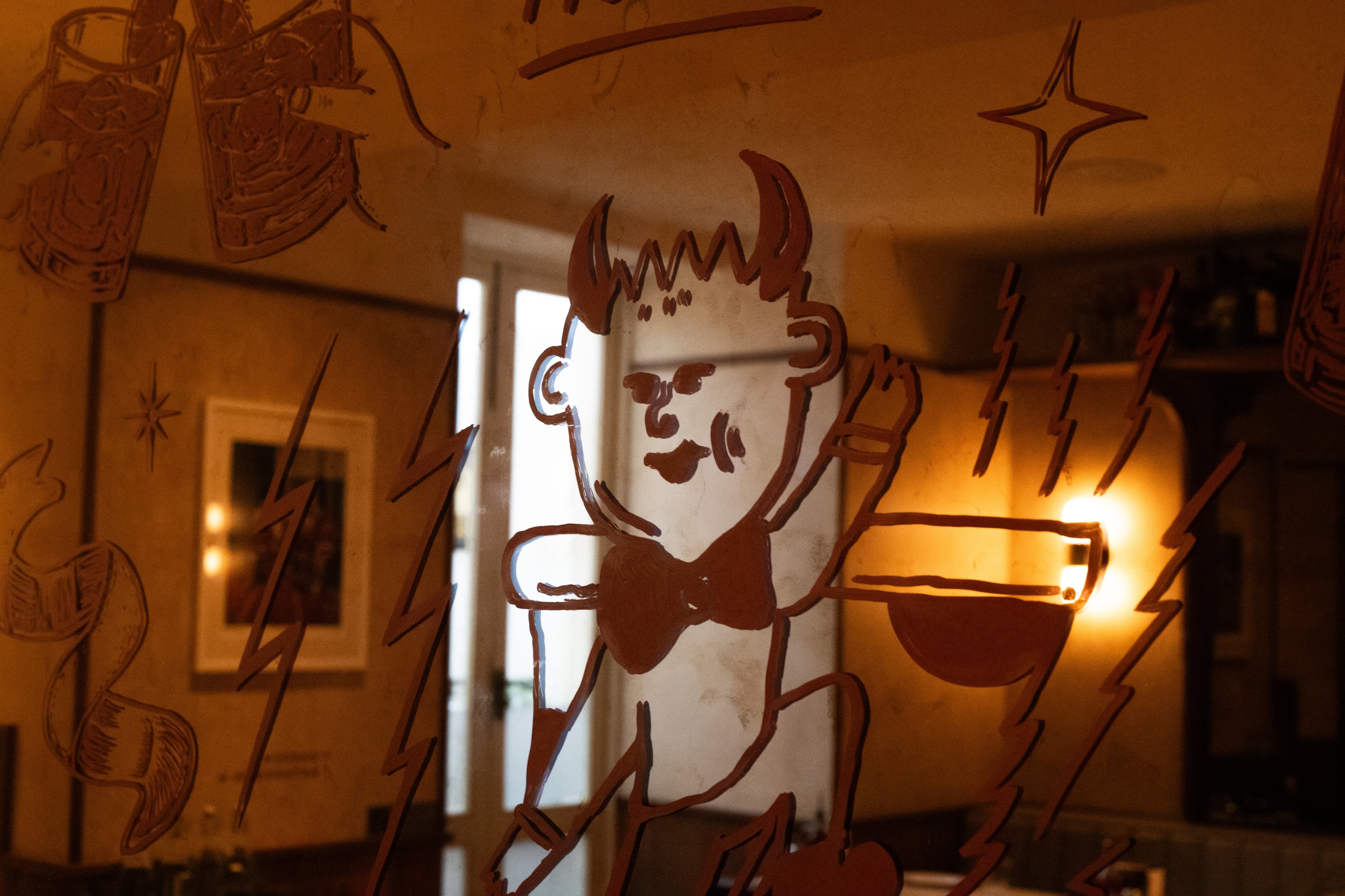 A close-up of playful hand-painted cocktail illustrations on a restaurant mirror.