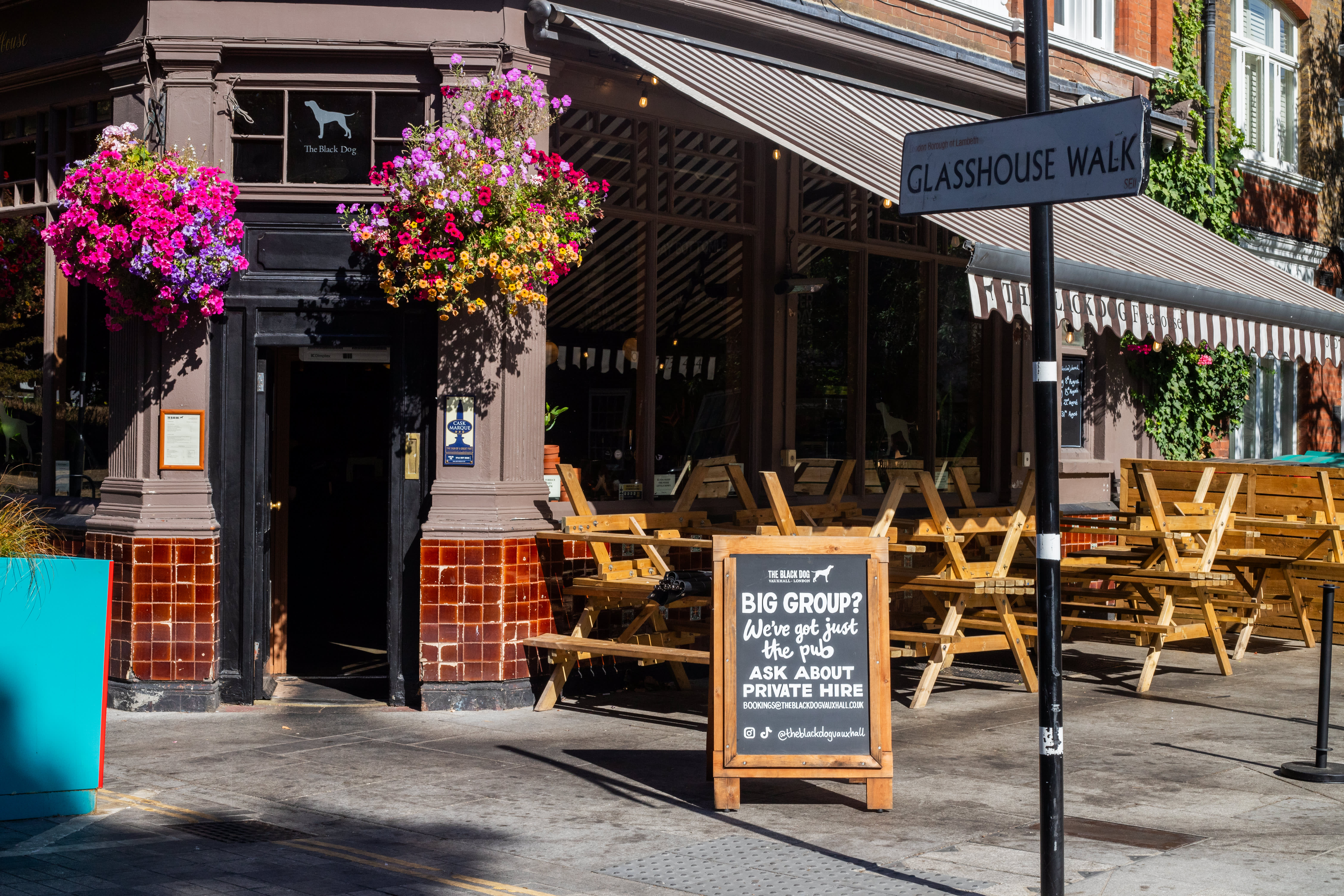 A hand-lettered A-board beside outdoor tables under The Black Dog pub awning.