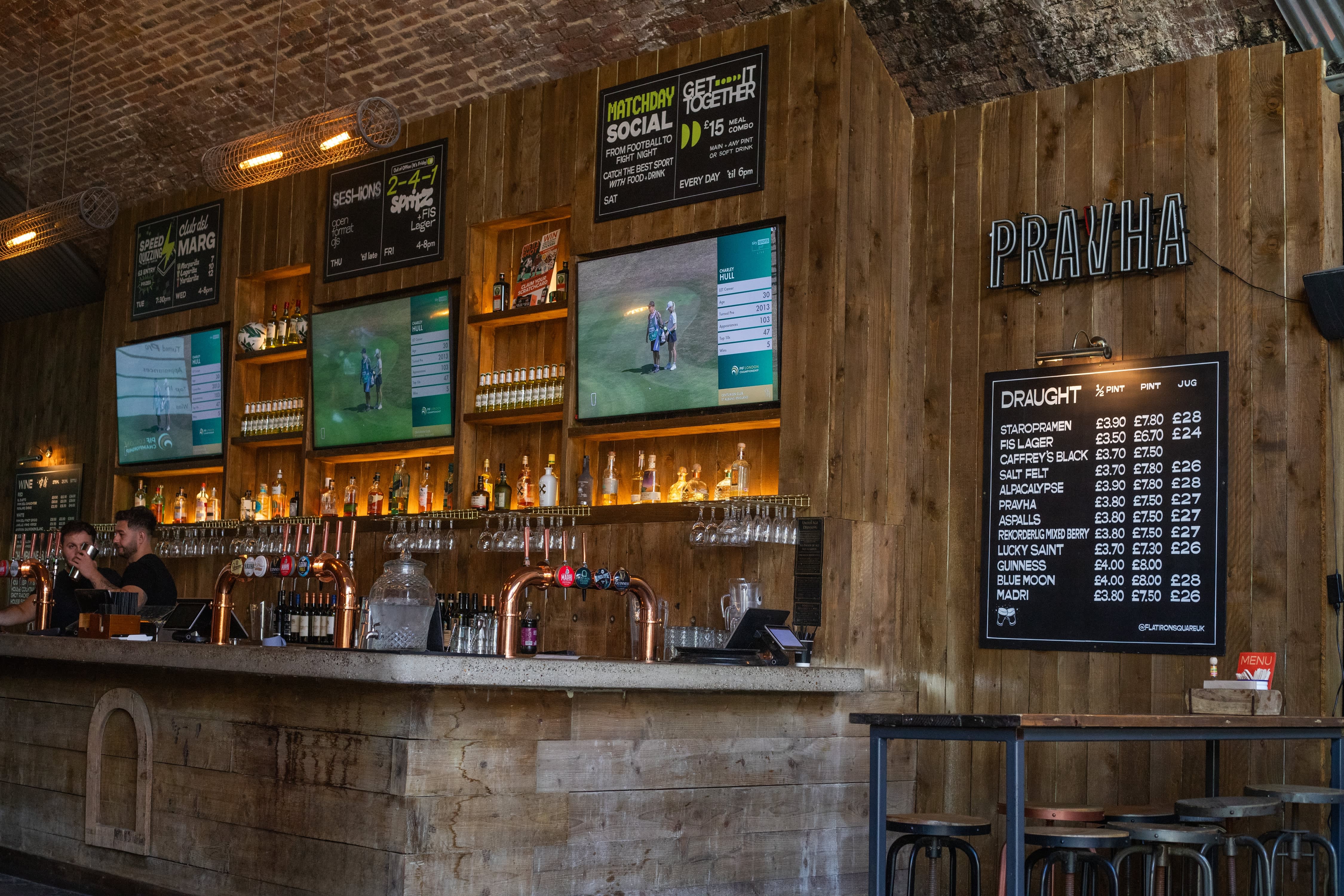 A bar wall with hand-lettered promotional menus and a framed draught beer blackboard.