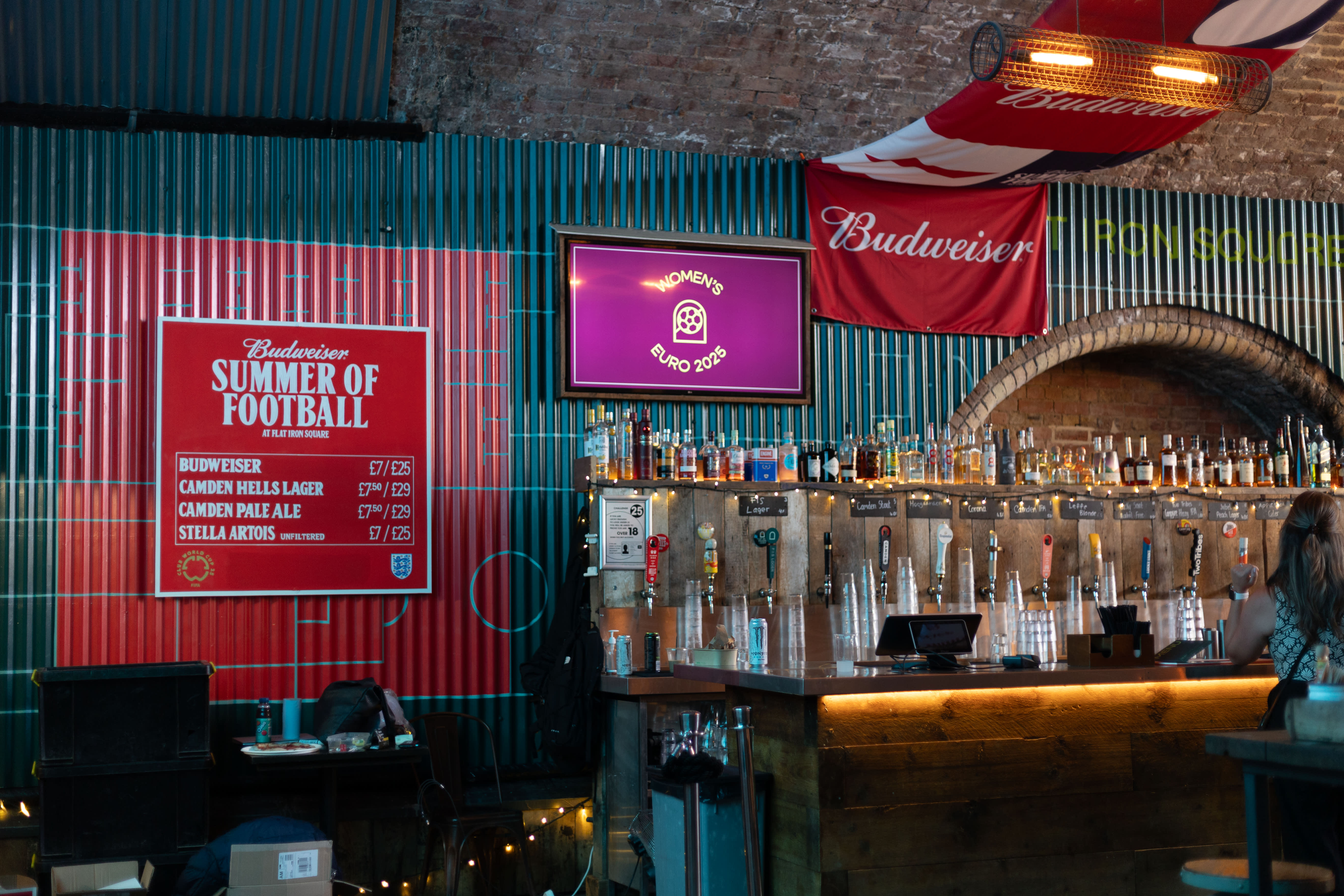 A Budweiser Summer of Football drinks menu and painted striped wall behind a bar.