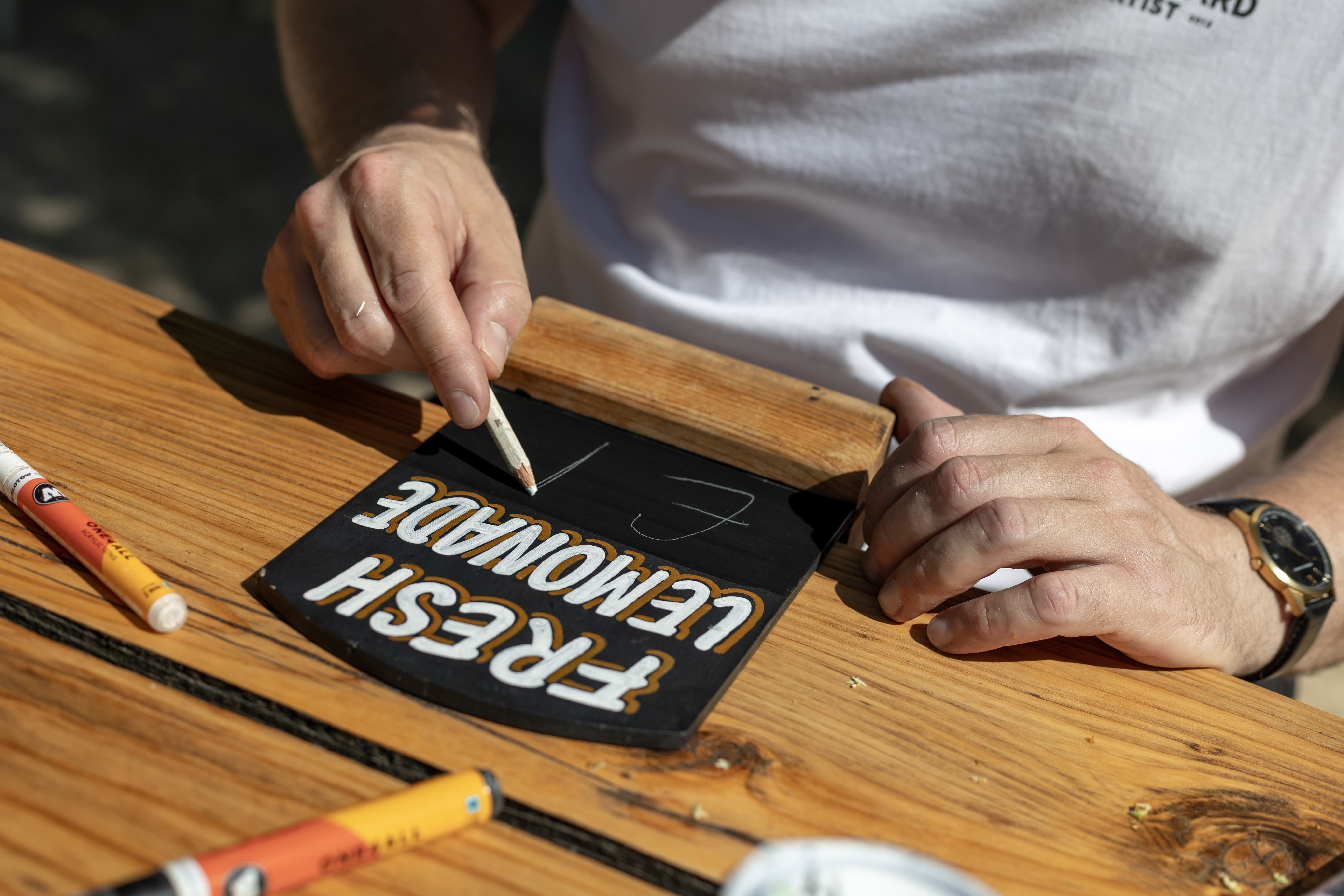 An artist painting white Fresh Lemonade lettering onto a small blackboard.
